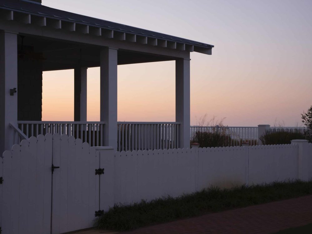 Modern house with a white fence and sunset sky in the background.