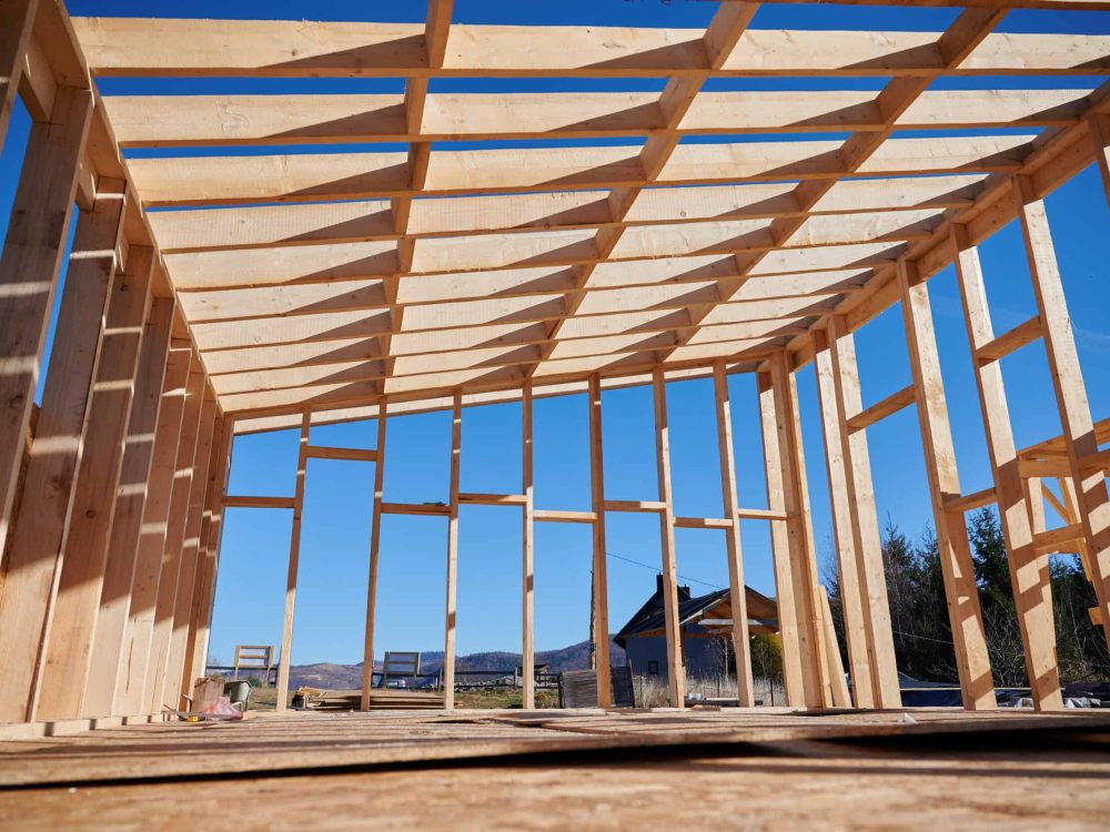 Wooden house frame under construction with clear blue sky.